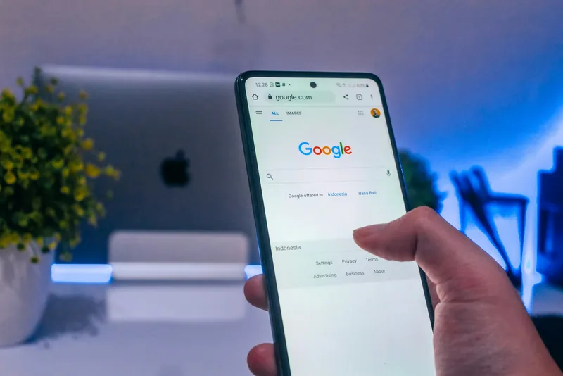 A hand holding a phone with the Google search page open